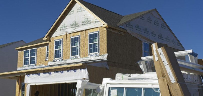 A house under construction with plywood walls and stacked windows